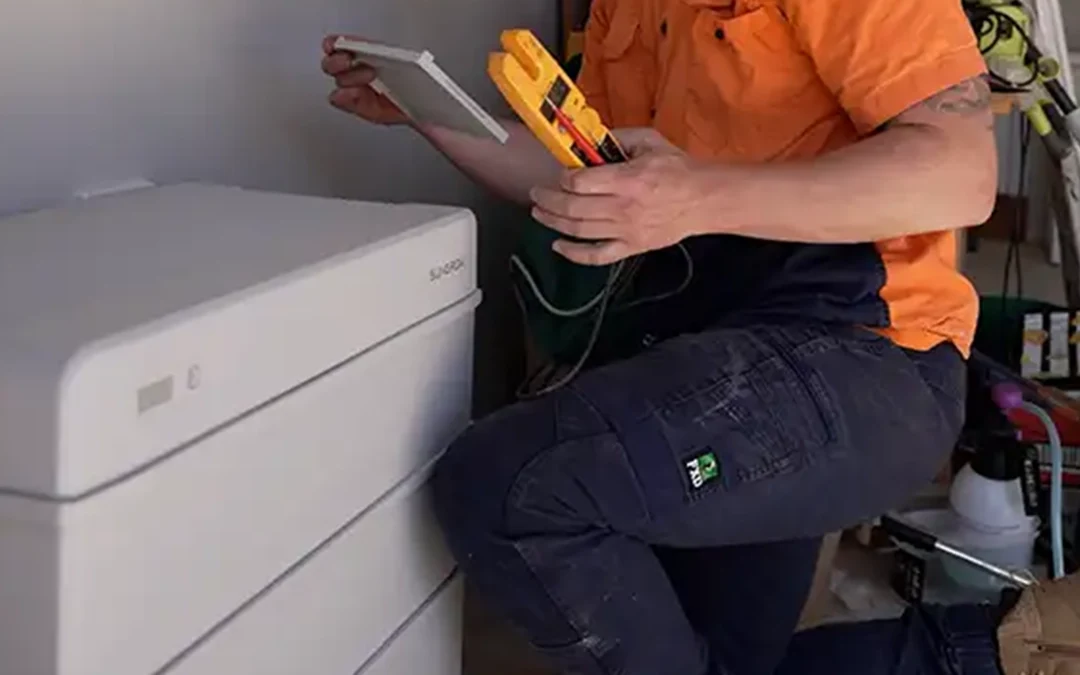 Installer commissioning a home battery beside an existing solar inverter